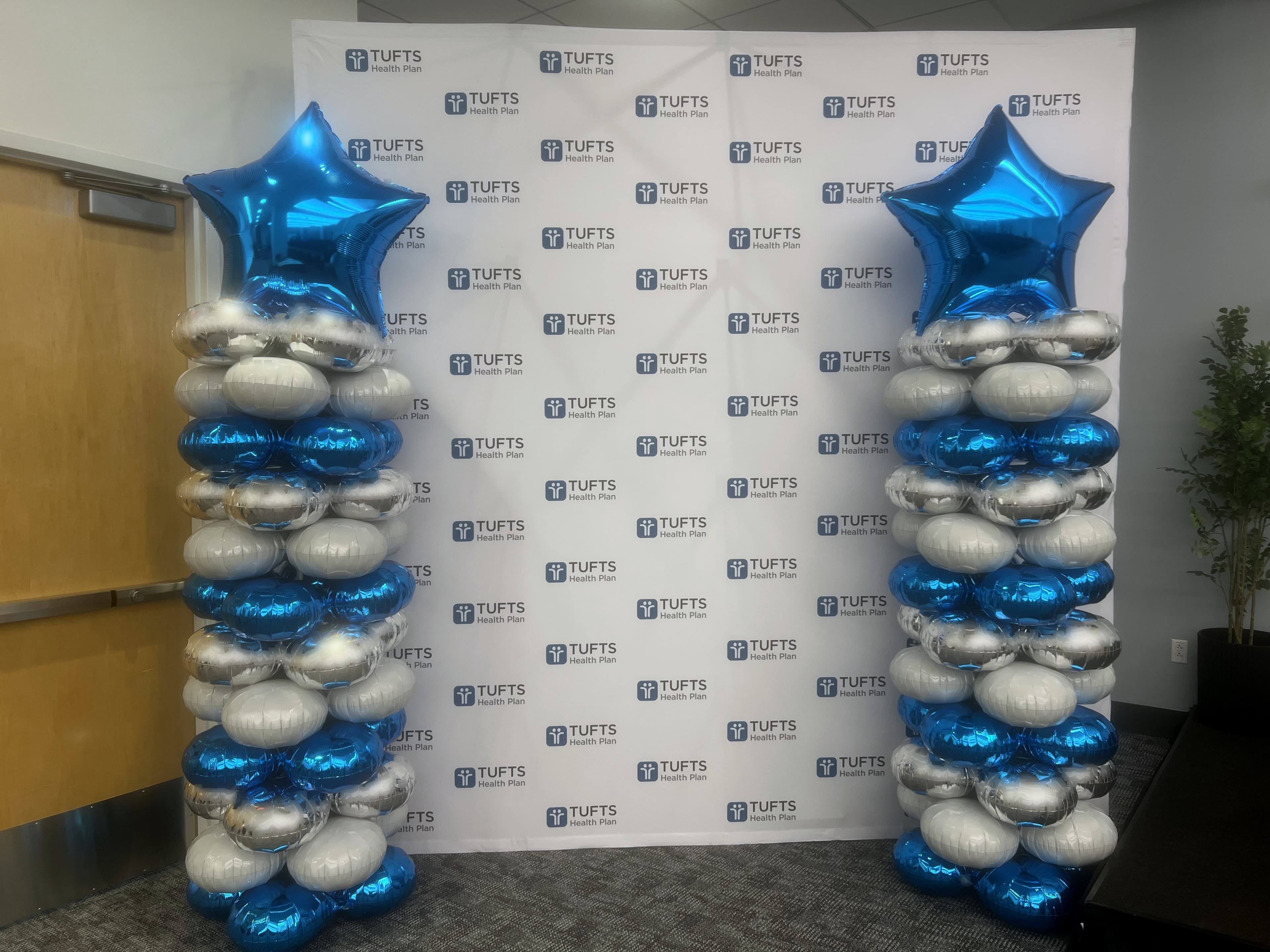 Blue and silver mylar balloon columns with foil star toppers flanking a Tufts Health Plan corporate step-and-repeat
