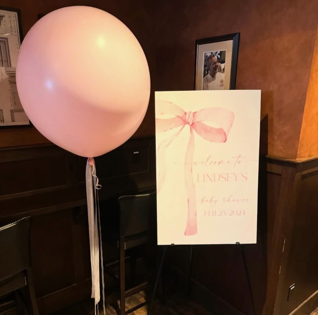 Welcome sign with pink bow graphic and a large pink balloon for a baby shower
