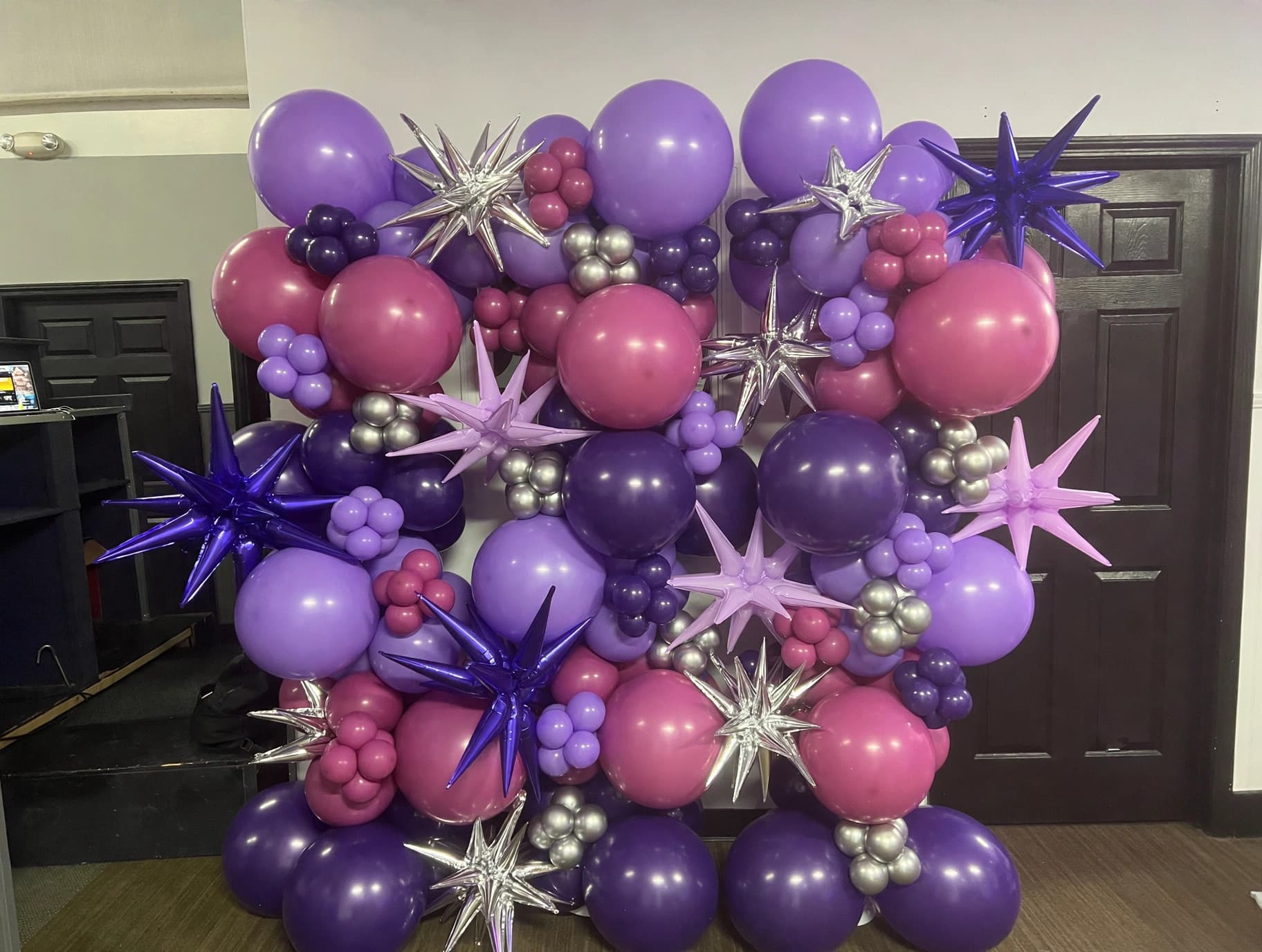Purple and pink starburst balloon wall with layered floral shapes