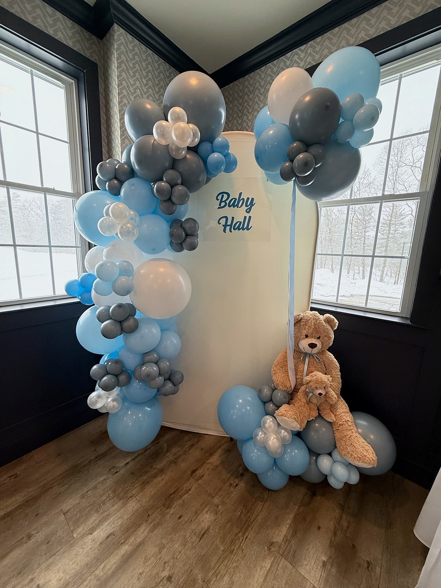 Blue, gray and white balloon garland around a Baby Hall arch backdrop with teddy bears