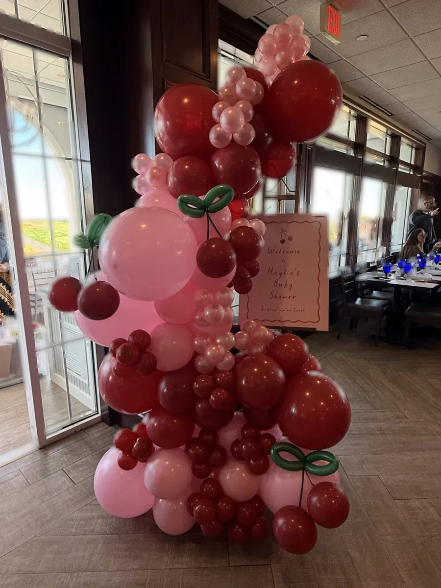Pink and red cherry themed balloon garland with custom welcome signage at a private dining venue