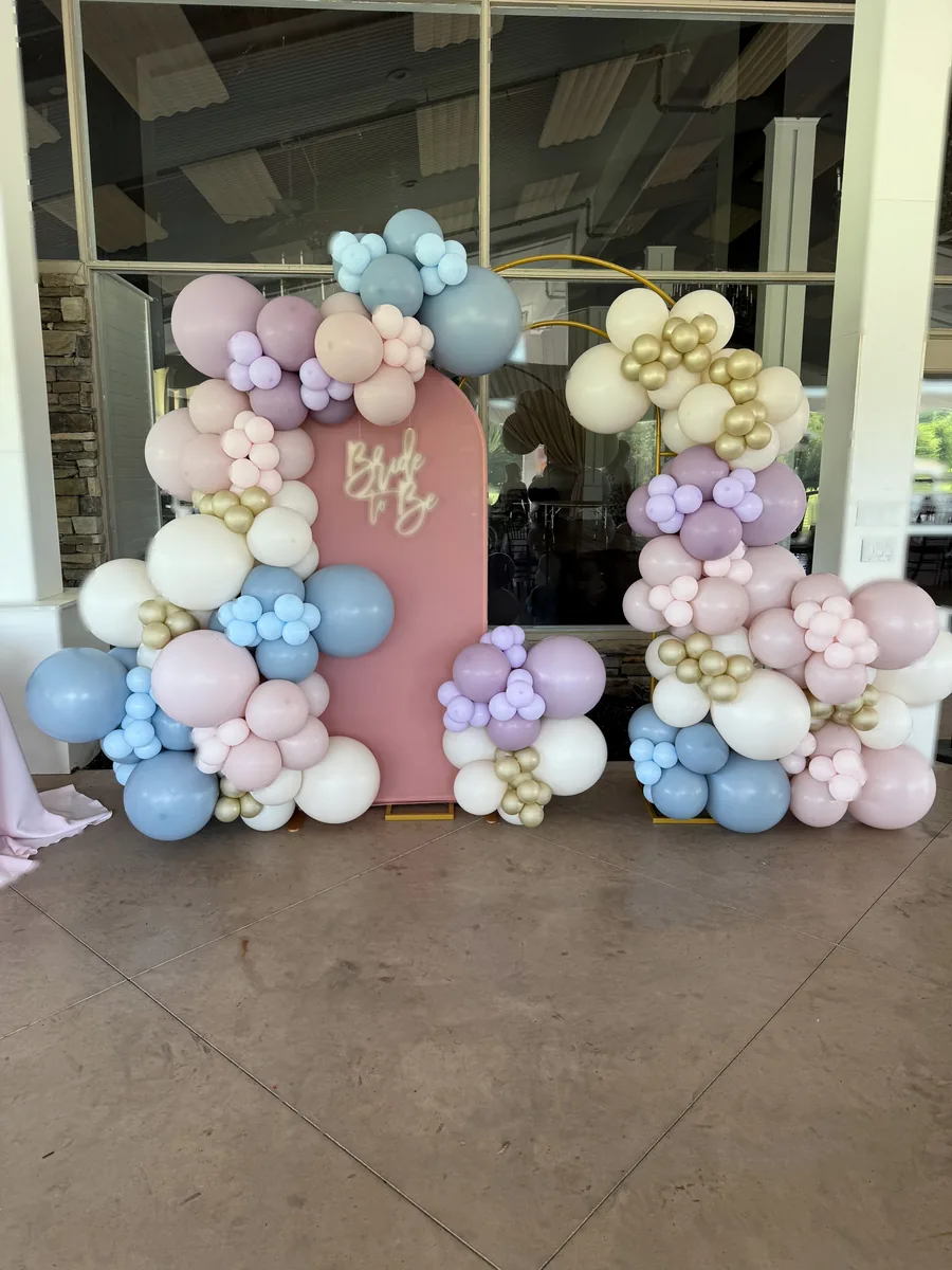 Pastel organic balloon garlands cascading across blush arched panels with acrylic Bride to Be lettering
