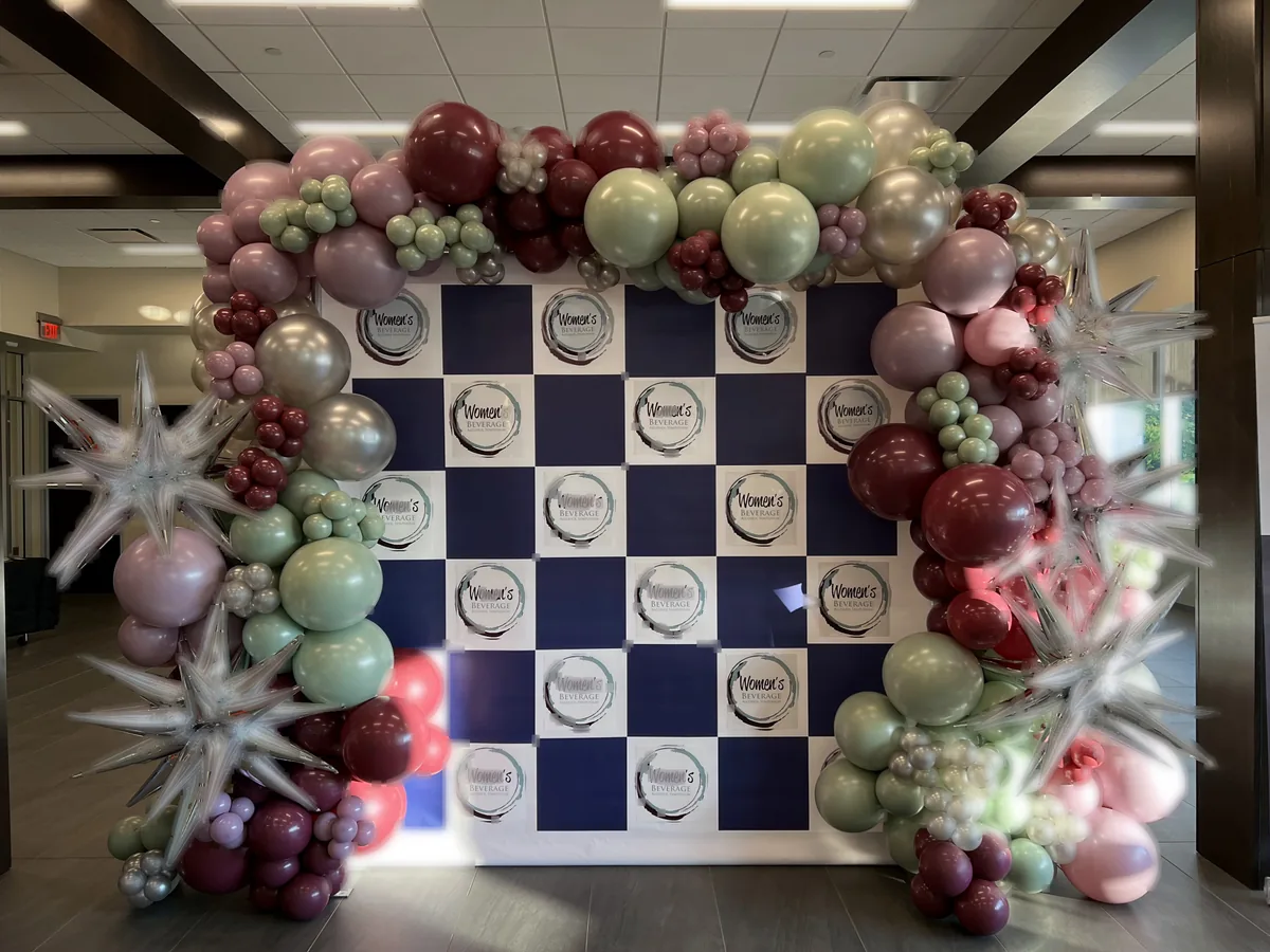 Burgundy, sage, and silver organic balloon garland framing a Women's Beverage Alcohol Symposium step-and-repeat backdrop