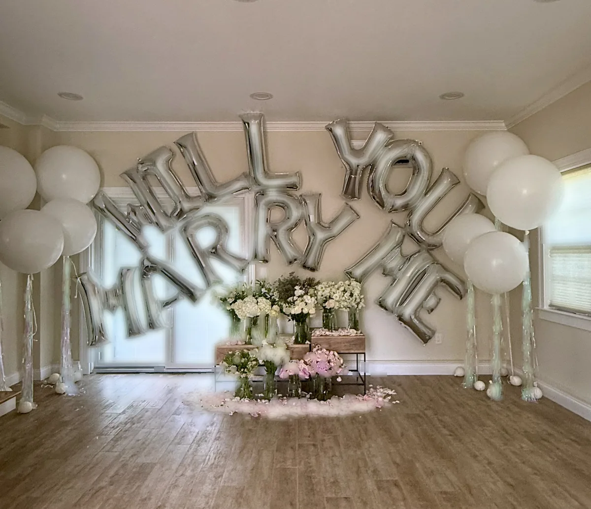 White organic balloon arch installation with cascading white latex clusters and bespoke fresh floral arrangements for an engagement proposal